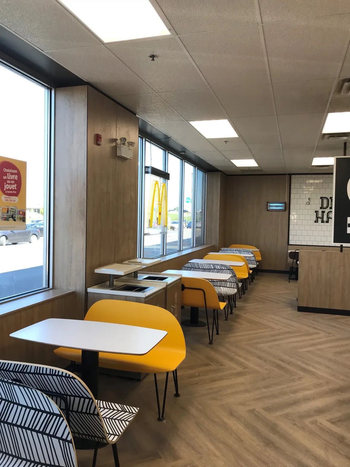 Une salle à manger McDonald's vide, avec des banquettes jaunes et des chaises à motifs disposées le long de baies vitrées.