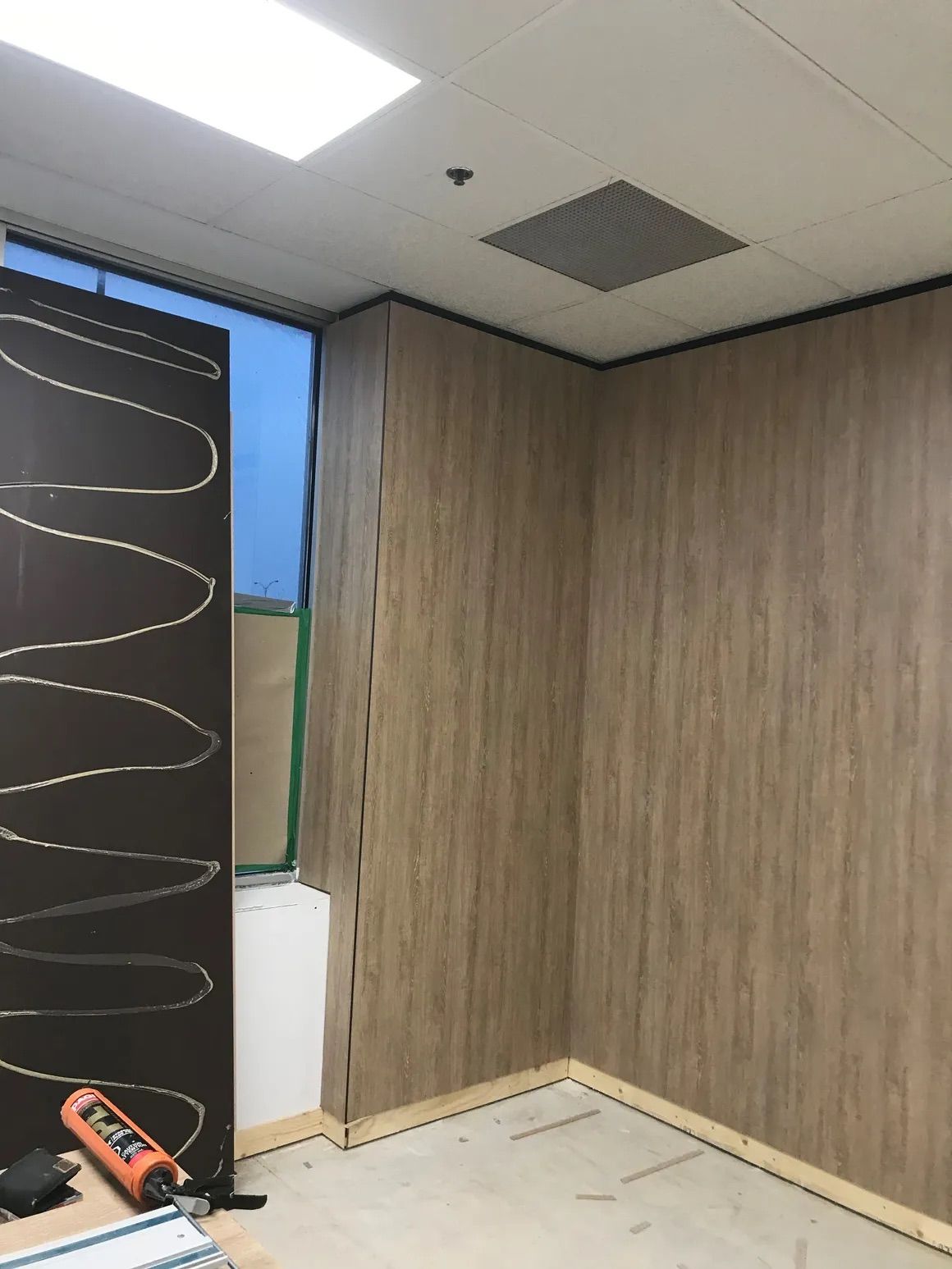 Murs lambrissés en construction dans une pièce, avec un panneau foncé partiellement installé et des lignes de colle visibles.
