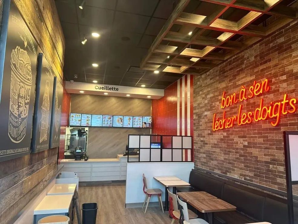 L'intérieur d'un restaurant moderne avec un mur de briques orné d'une enseigne rouge néon, des tables en bois et un comptoir de service.