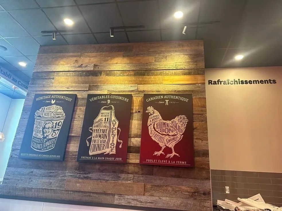Trois affiches encadrées représentant une boisson, un tablier et un poulet sont accrochées à un mur lambrissé, avec l'inscription « Rafraichissements ».
