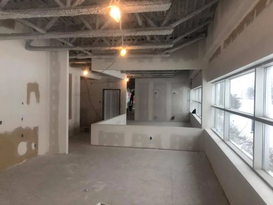 Vue intérieure d'un espace commercial en construction, avec cloisons sèches, solives de plafond apparentes et grandes fenêtres.