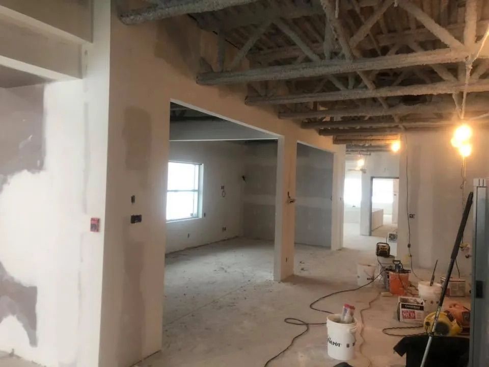 Un chantier intérieur avec des poutres en bois apparentes, des murs non peints et divers outils et seaux au sol.