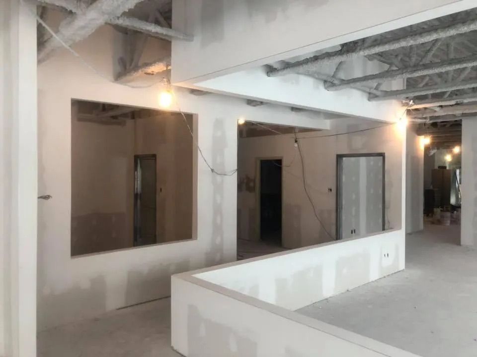Vue intérieure d'un espace commercial en construction, avec des murs en plaques de plâtre, des portes ouvertes et des solives de plafond apparentes.