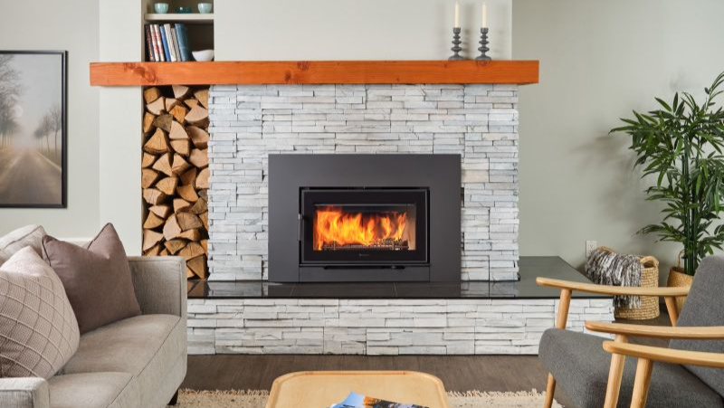 Wood fireplace insert with stacked firewood beside the hearth