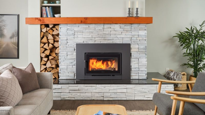 Wood fireplace insert with stacked firewood beside the hearth