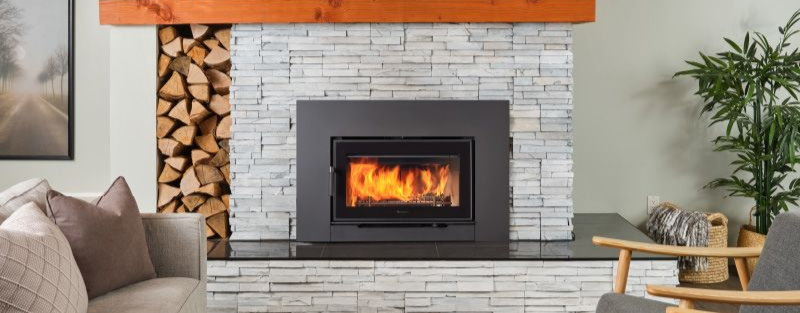 Wood fireplace insert with stacked firewood beside the hearth