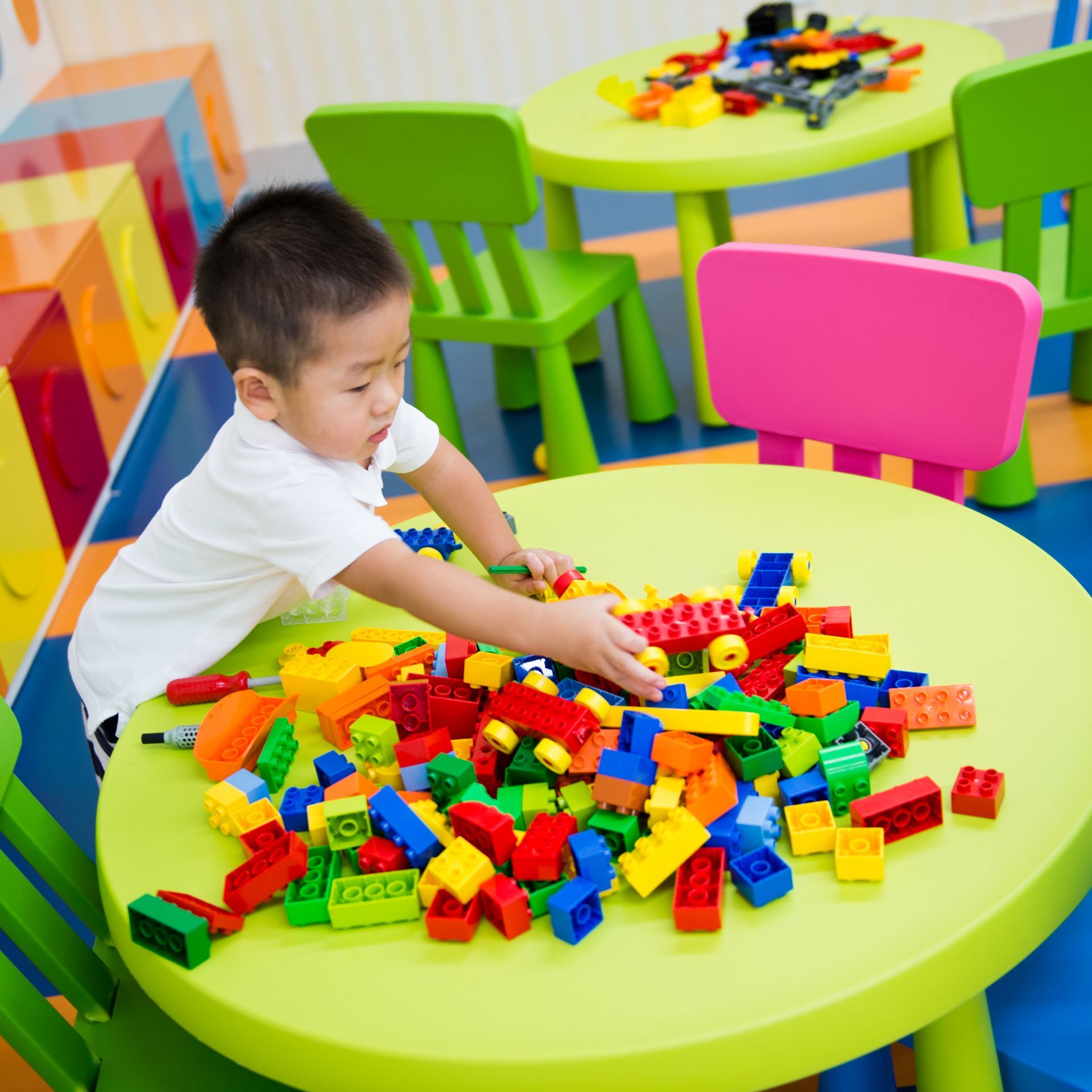 Boy playing with colorful building blocks on a green table in a playroom. Boy playing with colorful building blocks on a green table in a playroom.