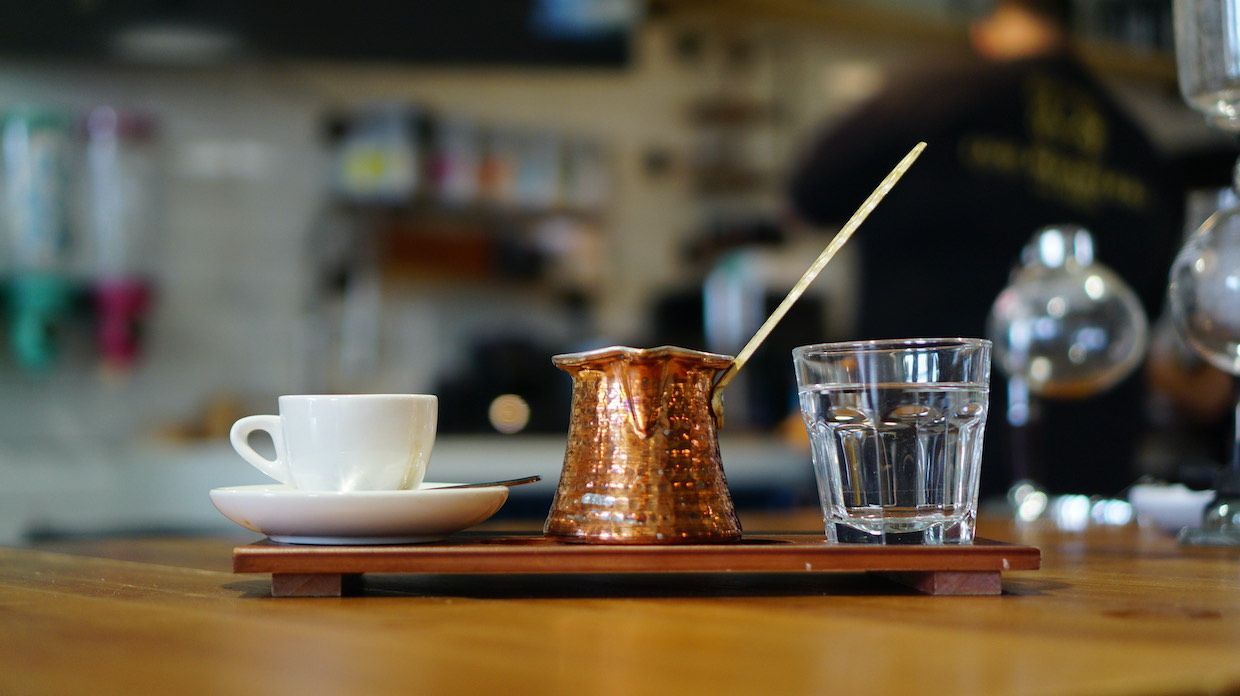 A cup of coffee and a glass of water on a wooden tray on a table.