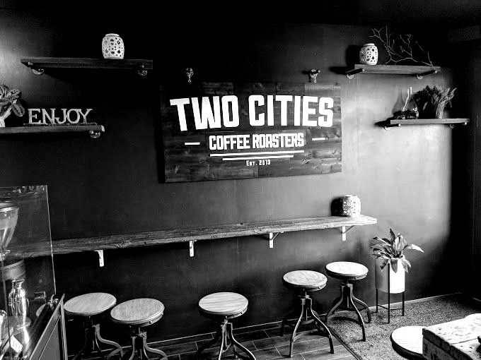 A black and white photo of a coffee shop with stools and a sign on the wall.