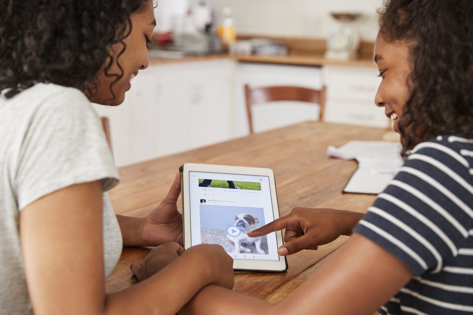 Two women are sitting at a table looking at a tablet.