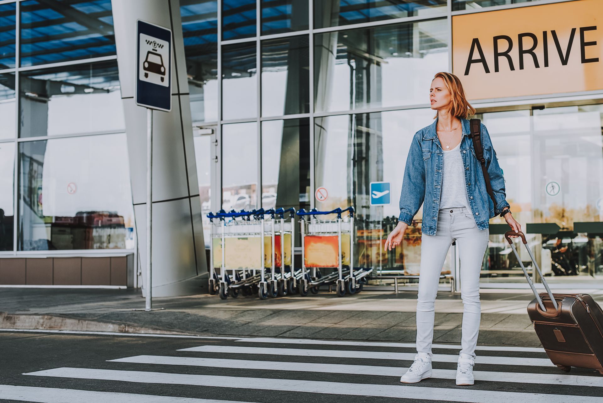 Woman with a suitcase at an airport crosswalk, looking towards the