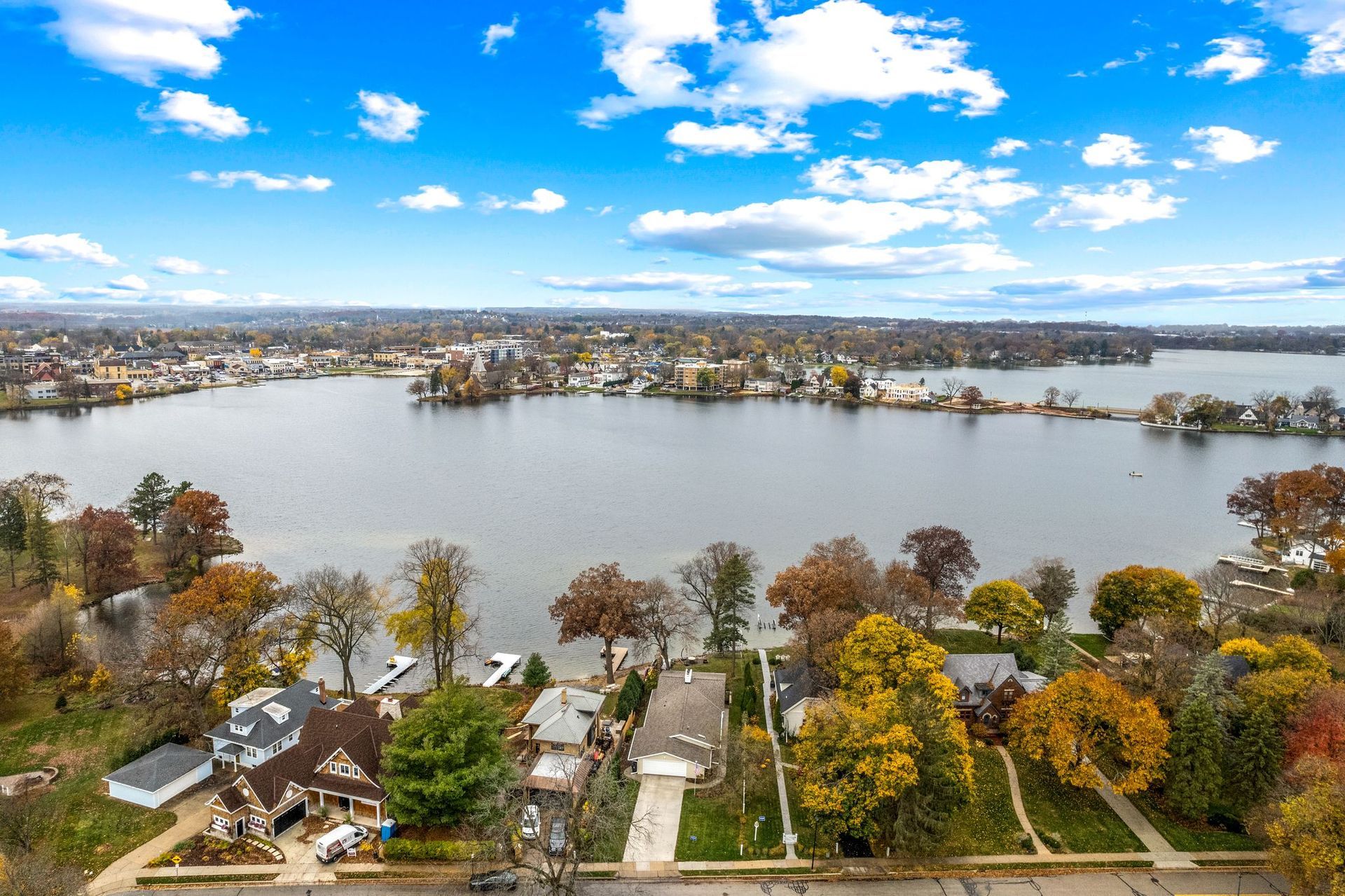 An aerial view of a lake and shoreline with houses and trees. Bright blue sky with clouds.