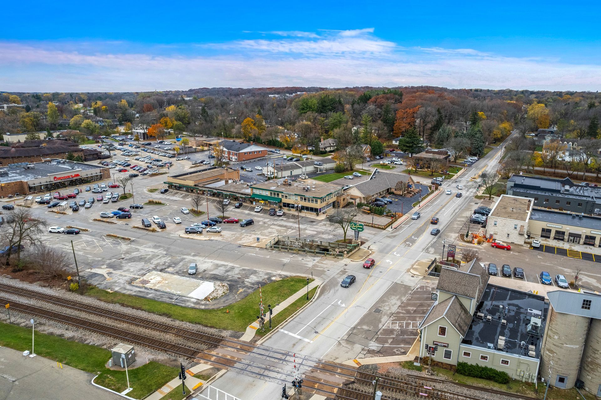 Aerial view of Elm Grove intersection with commercial buildings, parking lots, train tracks, and cars on the road.