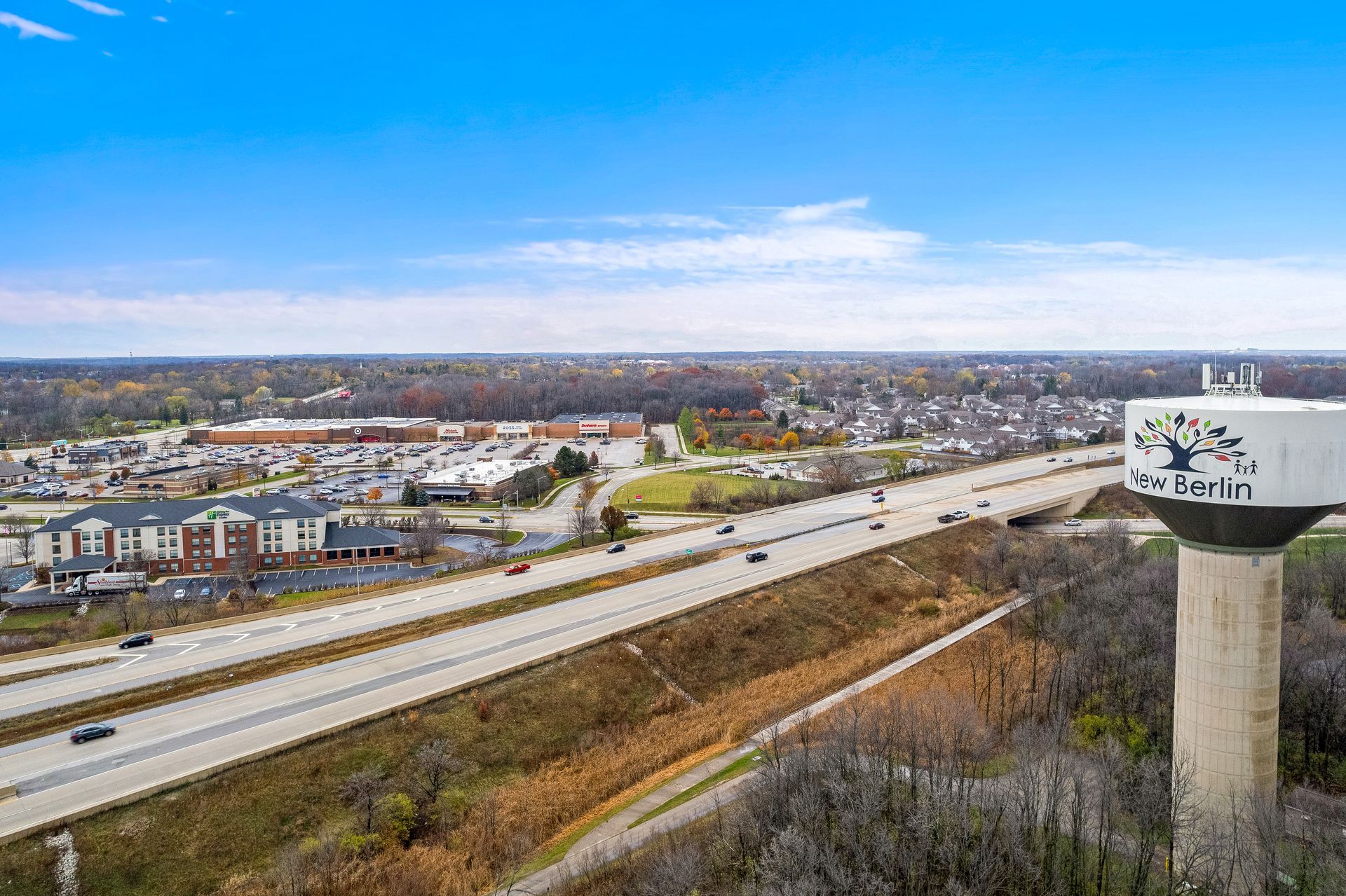 Aerial view of the city of New Berlin, WI, with a highway, buildings, and a water tower with the city's name on it.