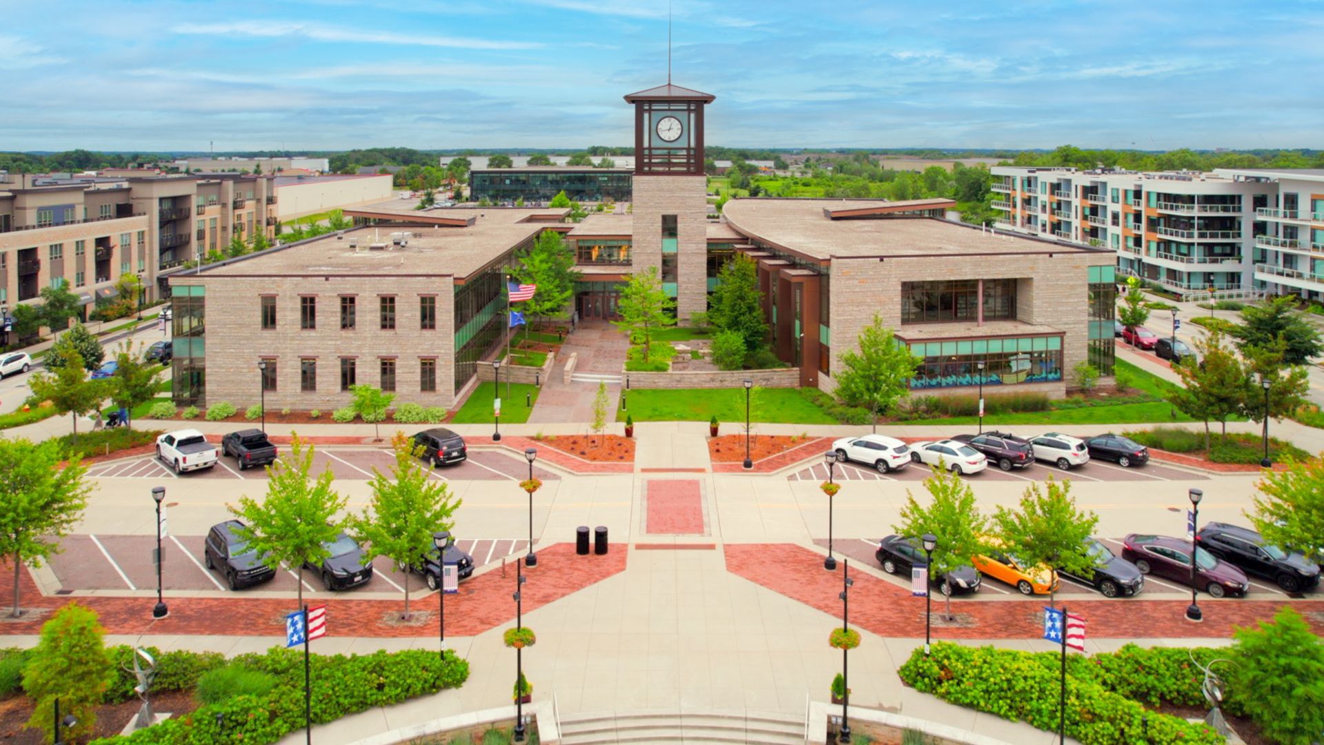 An aerial view of a brick building in Oak Creek Wisconsin with a clock tower and a plaza with parked cars and trees.
