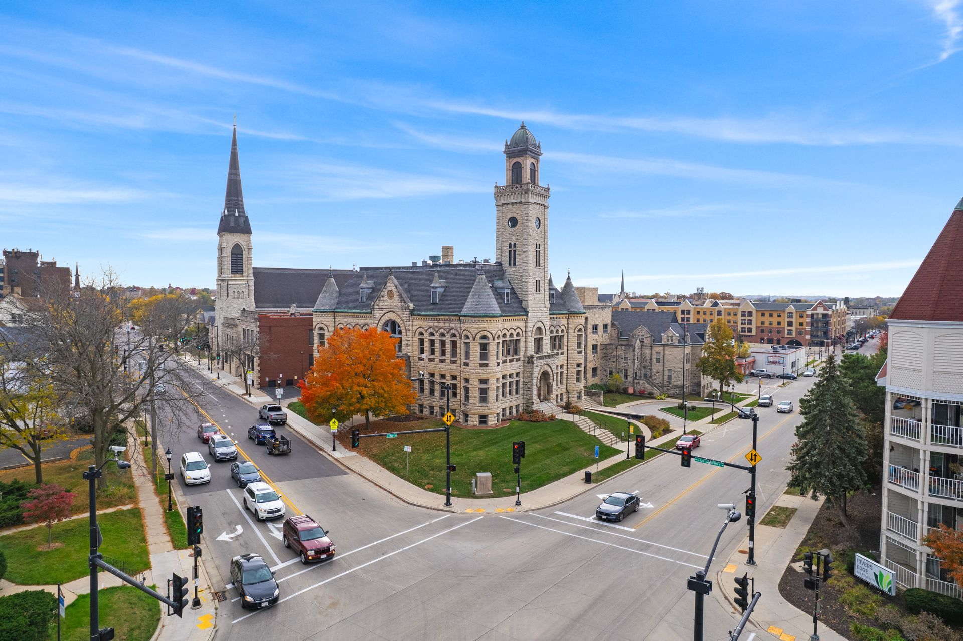 Street view of historic buildings in a city, with cars on the road and a blue sky.