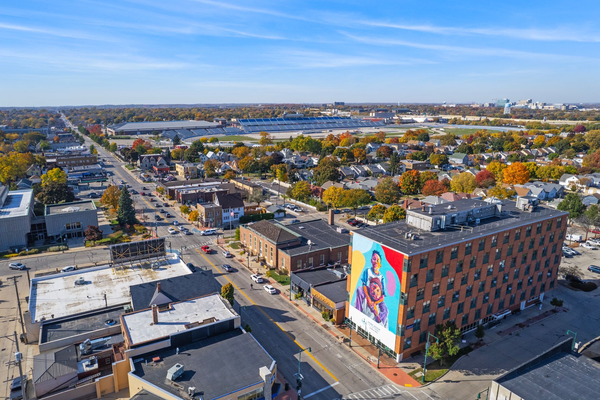 Aerial view of a city street with buildings and a large mural on the side of a brick building. Stadium in the distance.