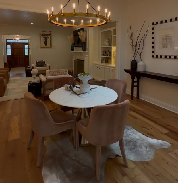 Elegant dining room with round marble table, four tan chairs, chandelier, and warm wood floors