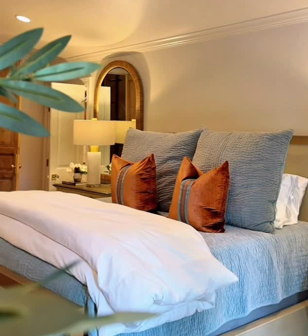 Cozy bedroom with a neatly made bed, blue bedding, orange accent pillows, and warm bedside lighting