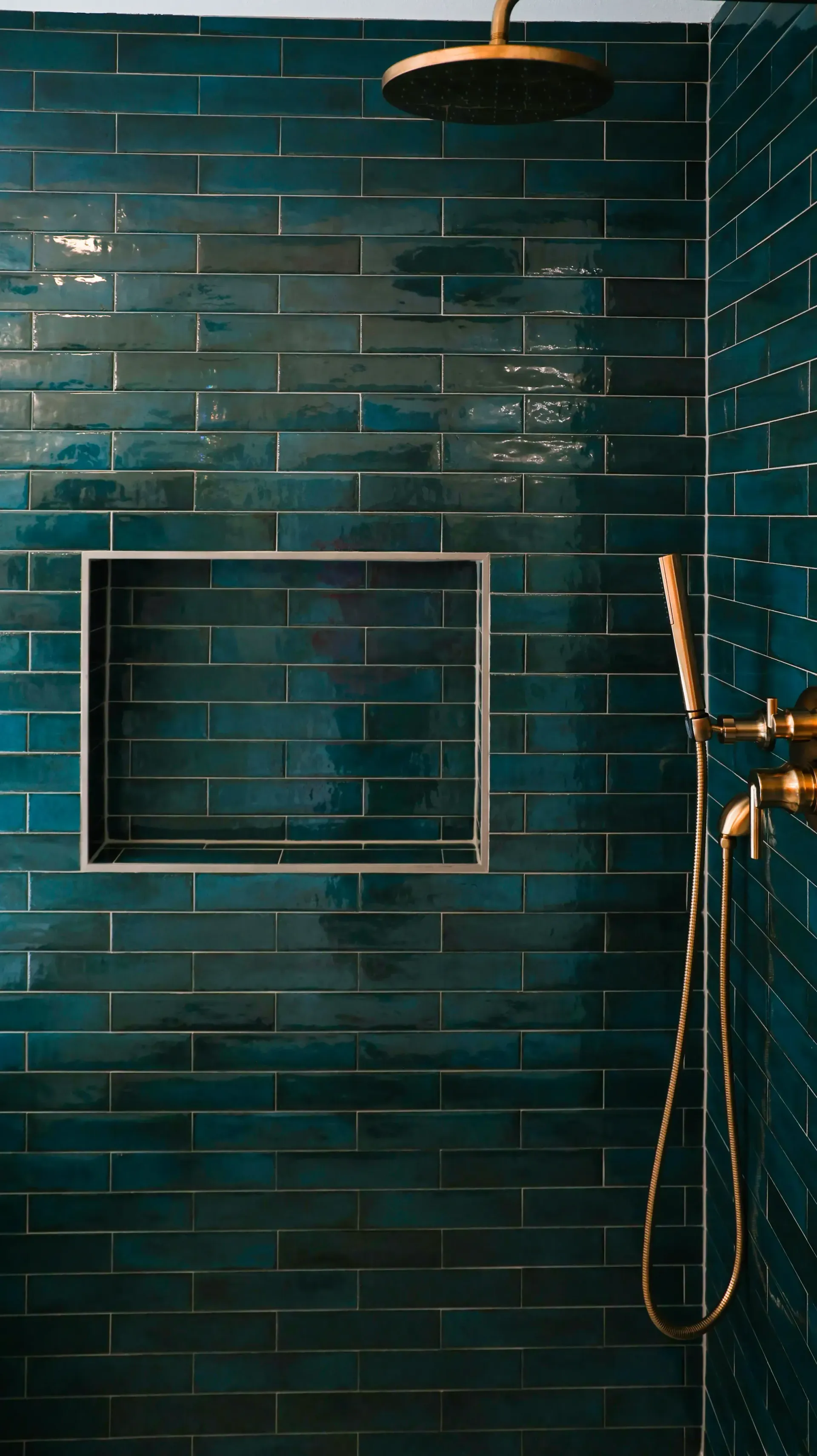 Dark teal tiled shower with a square niche, black showerhead, and gold fixture on the right.