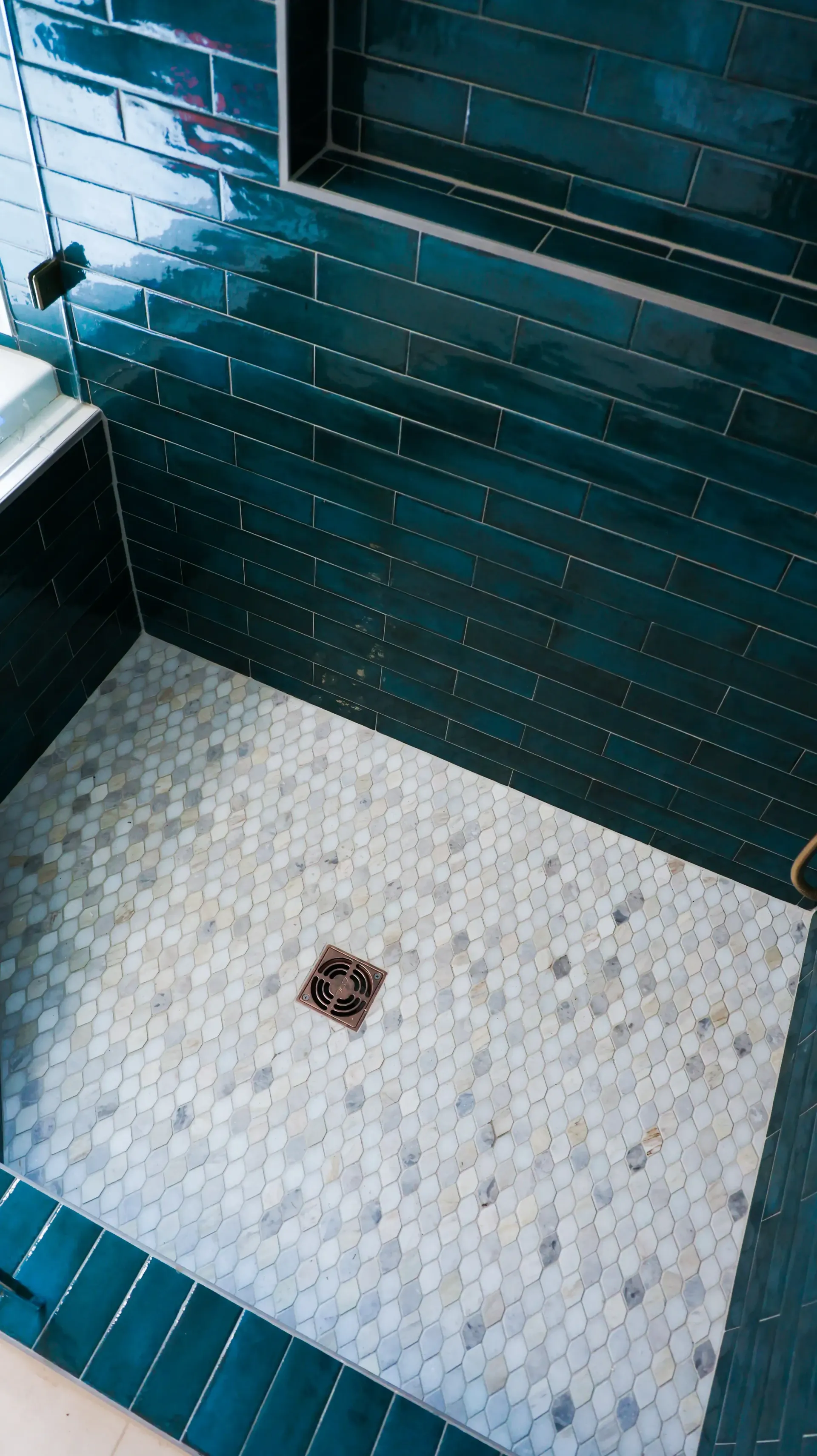 Small tiled shower stall with teal wall tiles, white floor tiles, and a central drain.