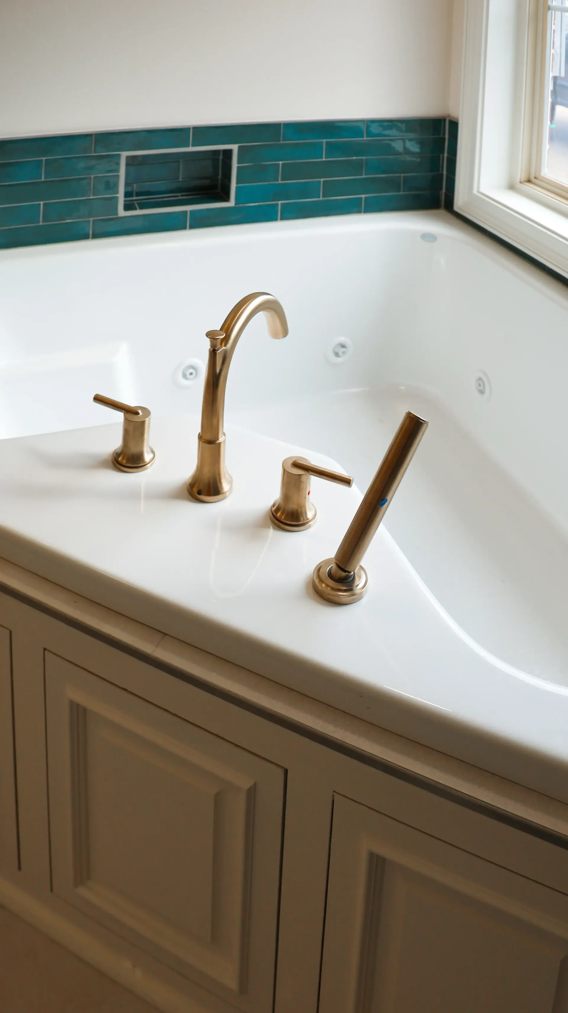 White bathroom vanity with a built-in sink, gold faucet, and teal tile backsplash by a window