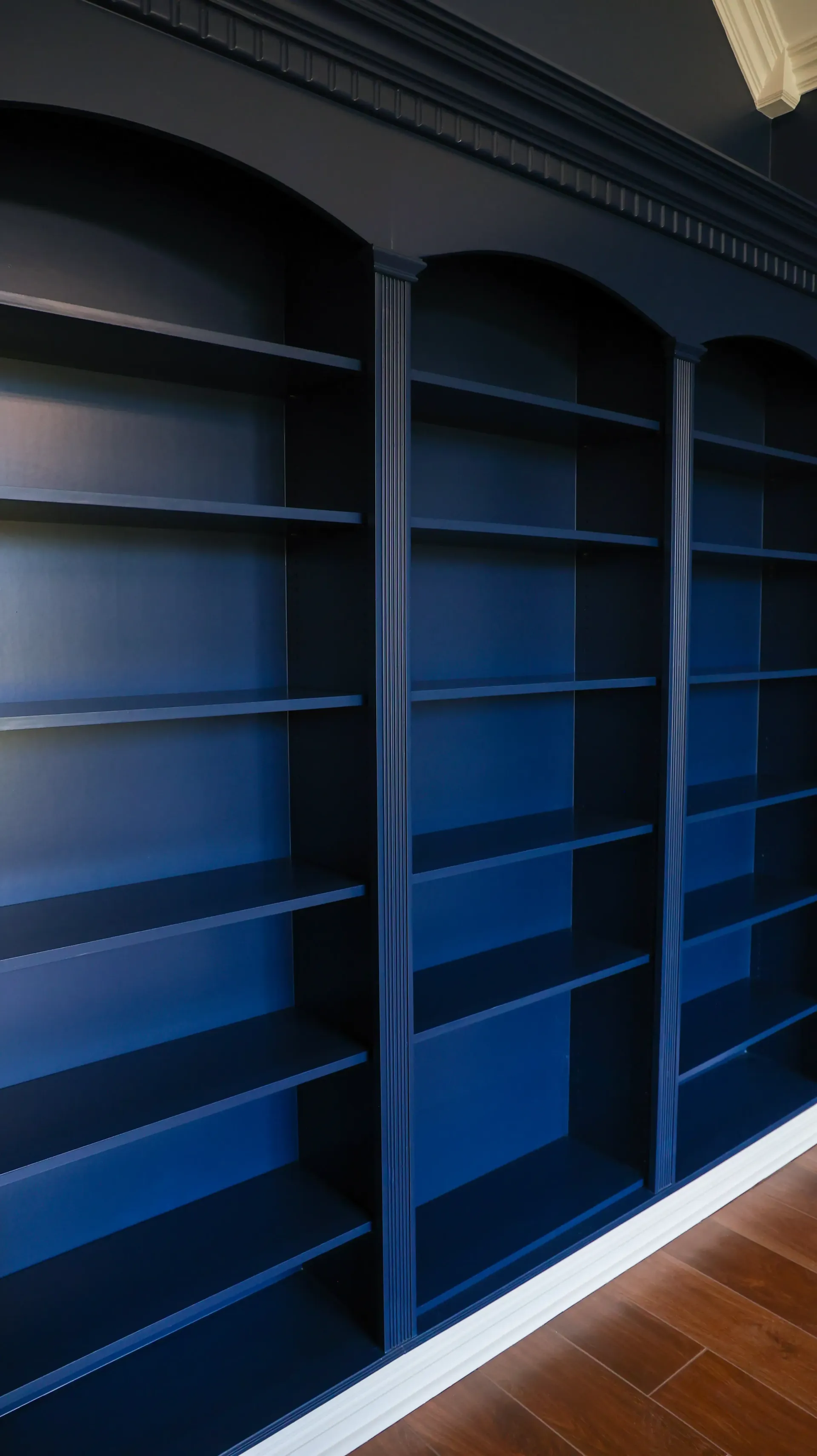 Built-in navy blue bookshelves along a wall with wood floor and white trim.