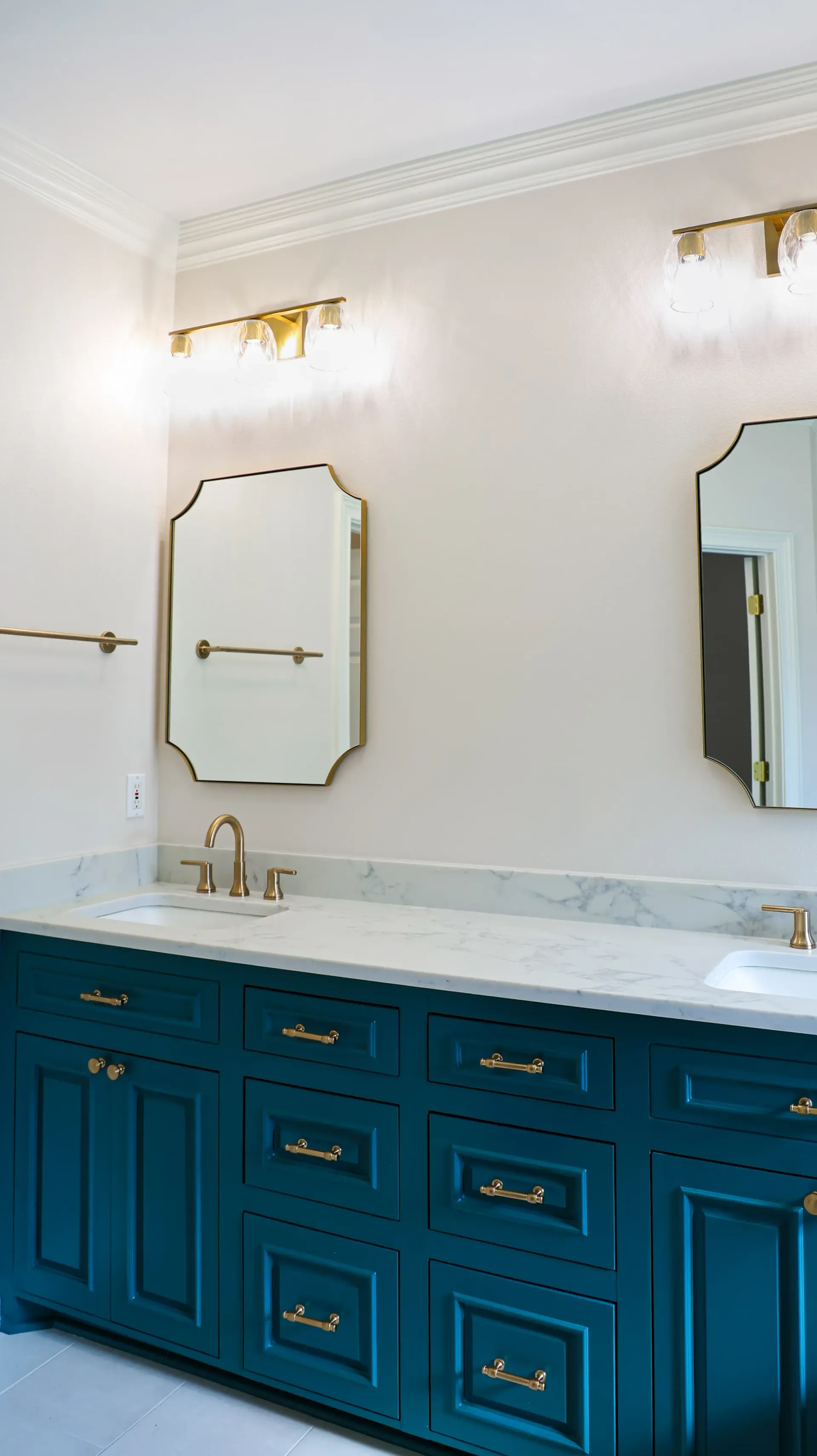 Elegant bathroom vanity with teal cabinets, white countertop, and gold-framed mirrors and sconces.