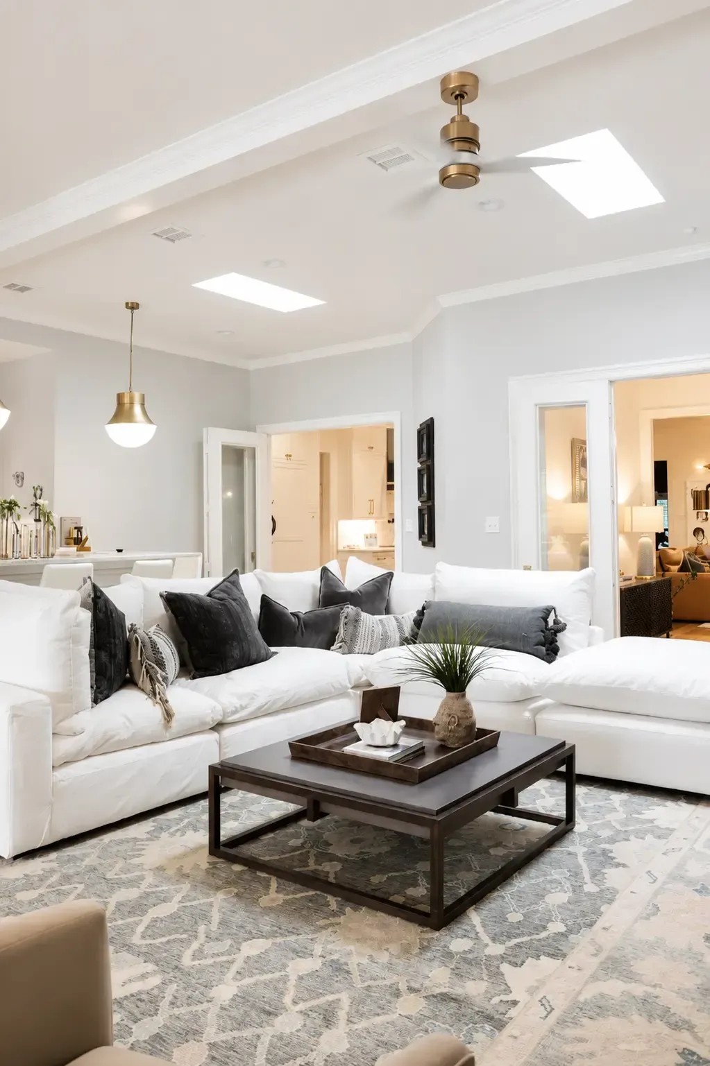 Bright living room with white sectional sofa, dark coffee table, patterned rug, and vaulted ceiling with skylights
