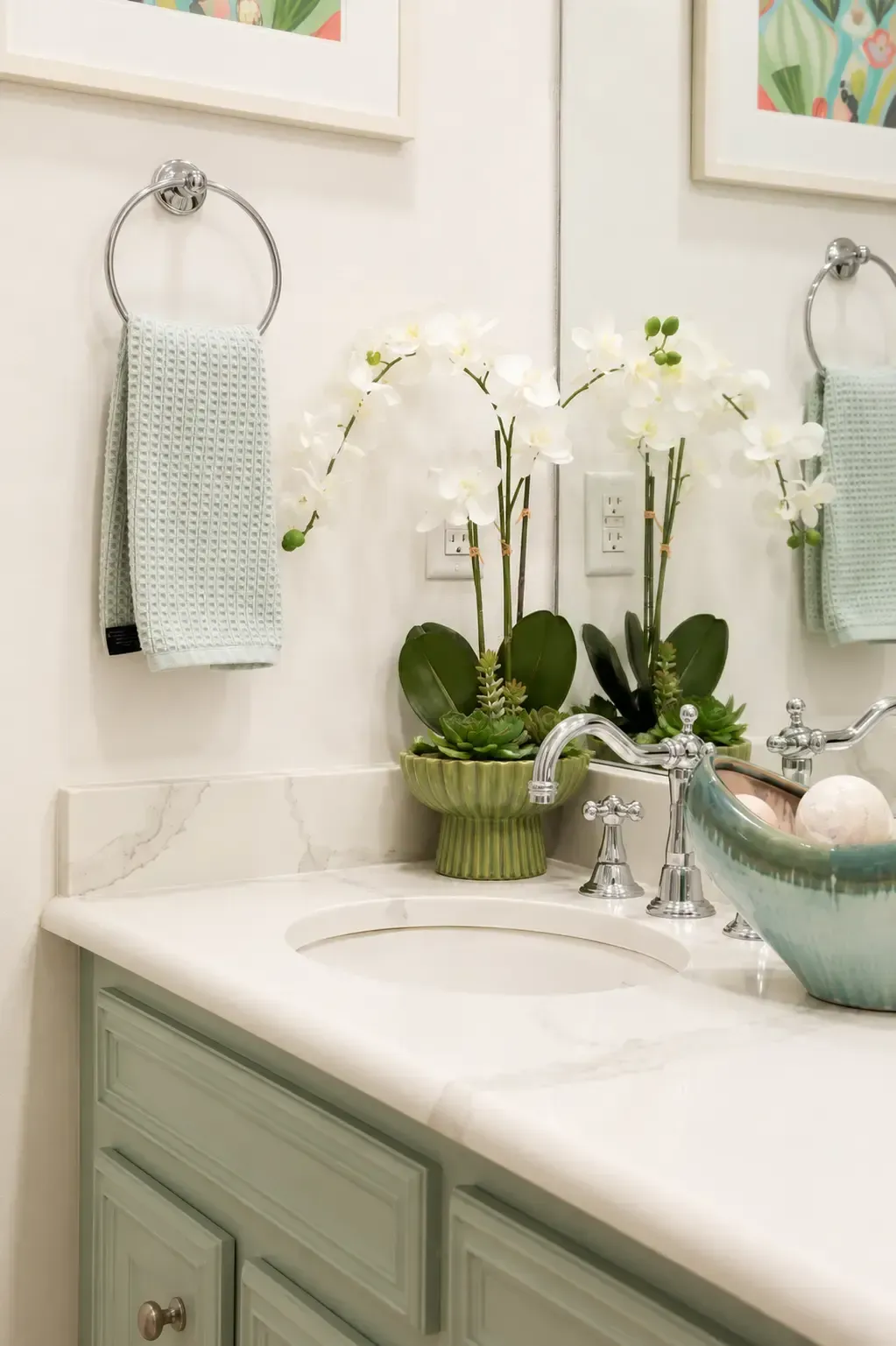 Mint-green bathroom vanity with white sink, orchid, and towel beside a mirror