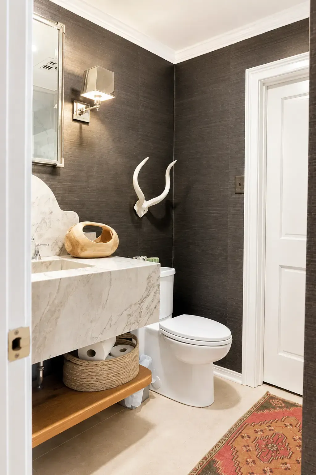 Small bathroom with dark walls, white toilet and vanity, woven basket, and patterned rug.