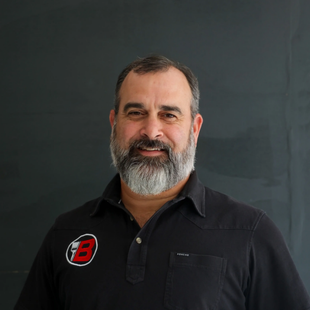 Portrait of a smiling man with a gray beard in a black polo shirt against a dark background