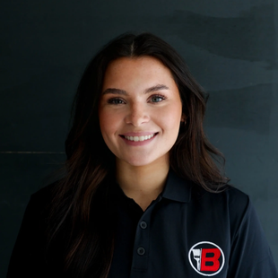 Portrait of a smiling woman in a black shirt with a red-and-white logo on a dark background