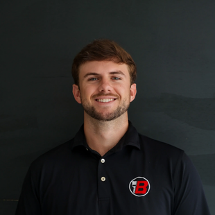 Smiling man in a black polo shirt with a red logo, standing against a dark background