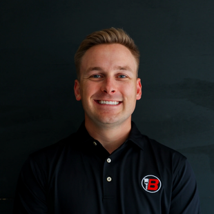 Portrait of a smiling man in a black polo with a red-and-white logo on a dark background