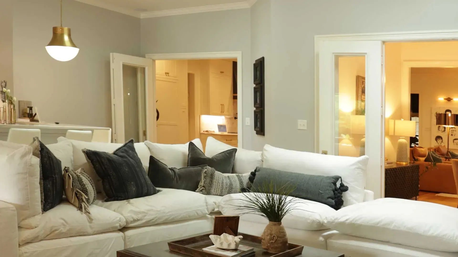 Bright living room with white sectional sofa, dark pillows, coffee table, and open doorways to adjoining rooms