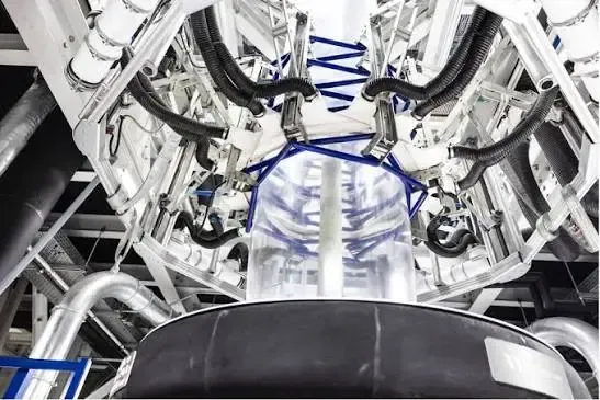 Industrial machine with white metal framework and blue cables surrounding a large cylindrical chamber