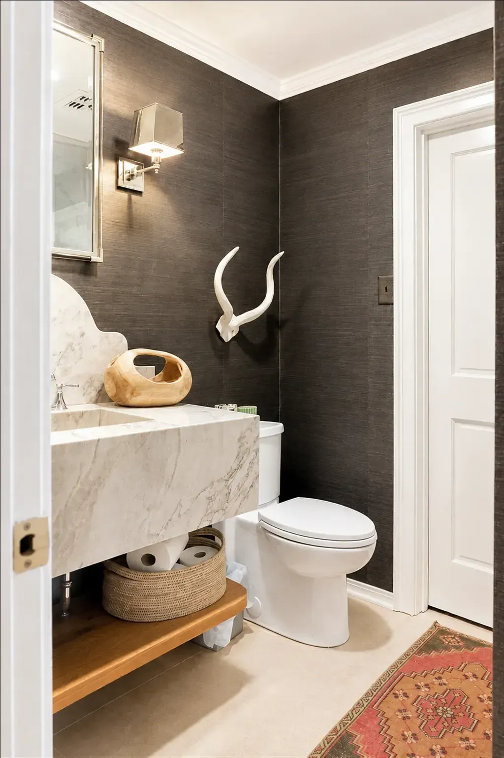 Small modern bathroom with dark walls, a marble vanity, white toilet, and a wicker basket.