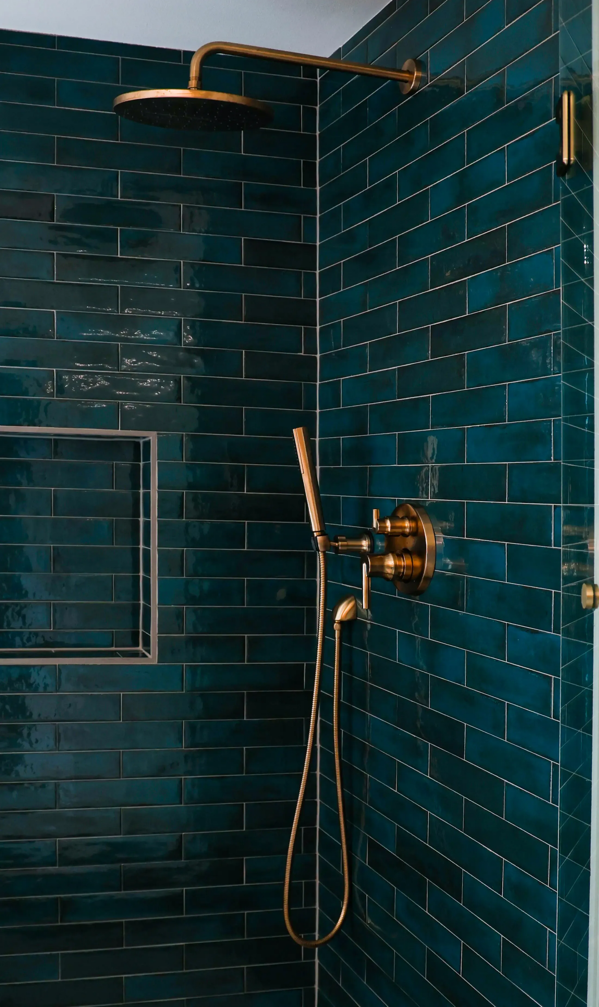 Teal-tiled shower with brass fixtures and a rain showerhead in a modern bathroom