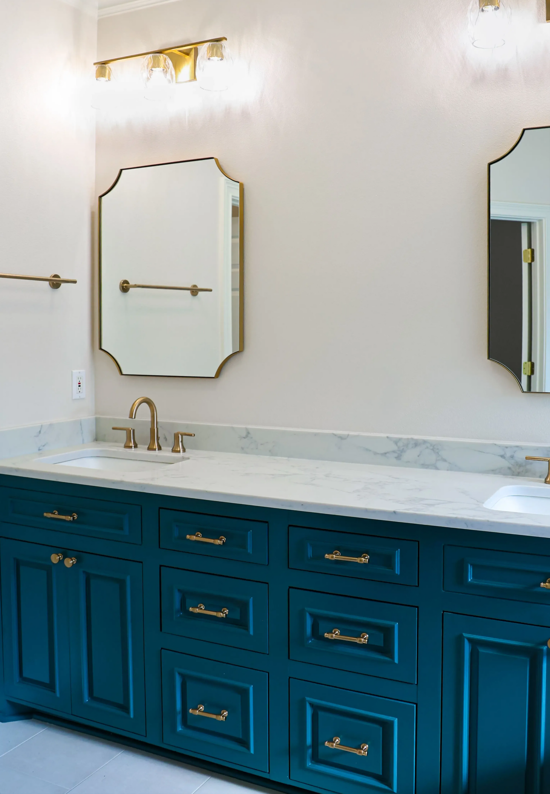 Blue vanity with white marble countertop and gold fixtures in a bright bathroom, with an octagonal mirror.