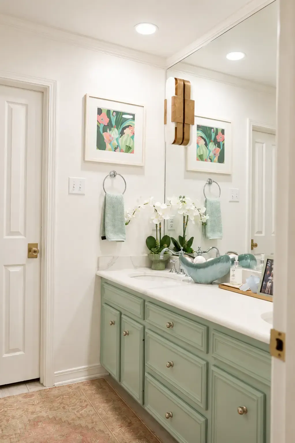 Bright bathroom vanity with mint green cabinets, white countertops, mirror, and floral art.