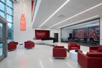 Modern Coca-Cola lounge with red chairs, white floors, and large branded wall display