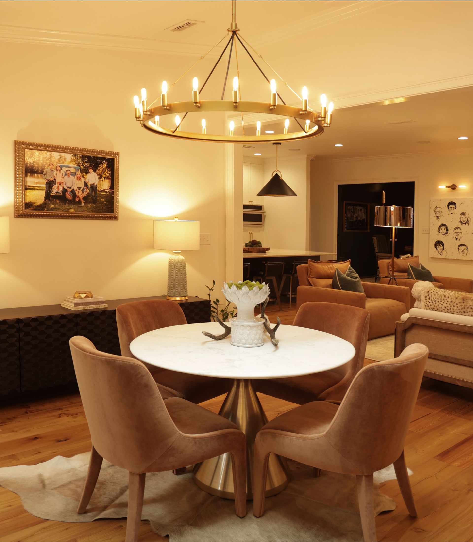 Cozy dining area with round white table, tan chairs, chandelier, and warm living room beyond