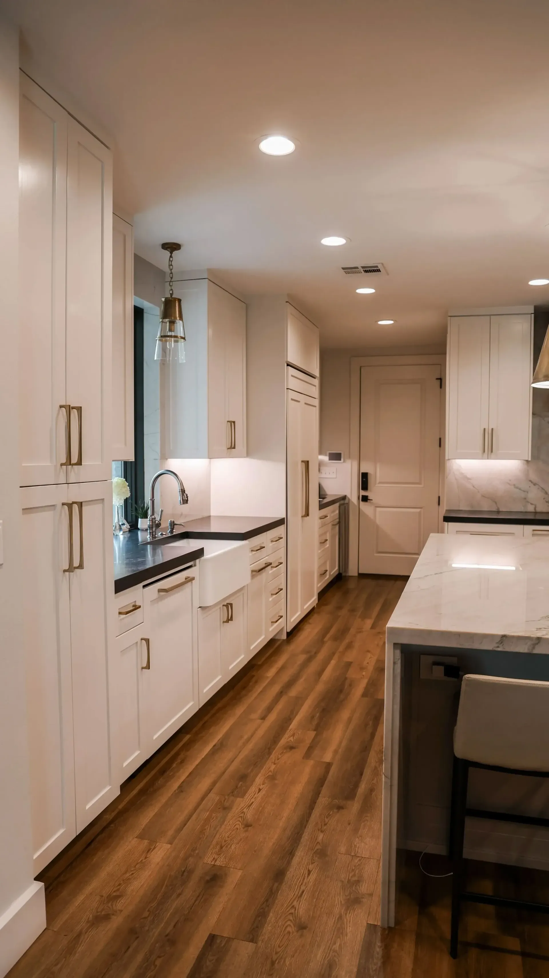 Bright modern kitchen with white cabinets, wood floors, island, and recessed ceiling lights