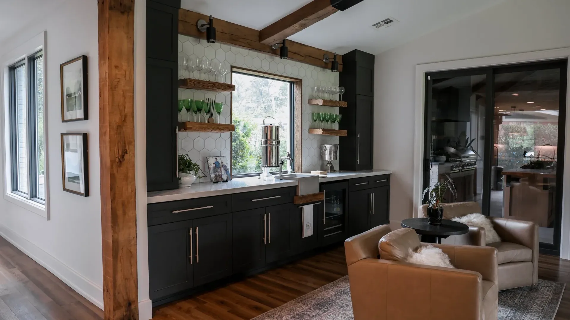 Modern kitchen and sitting area with dark cabinets, bar stools, and large windows.