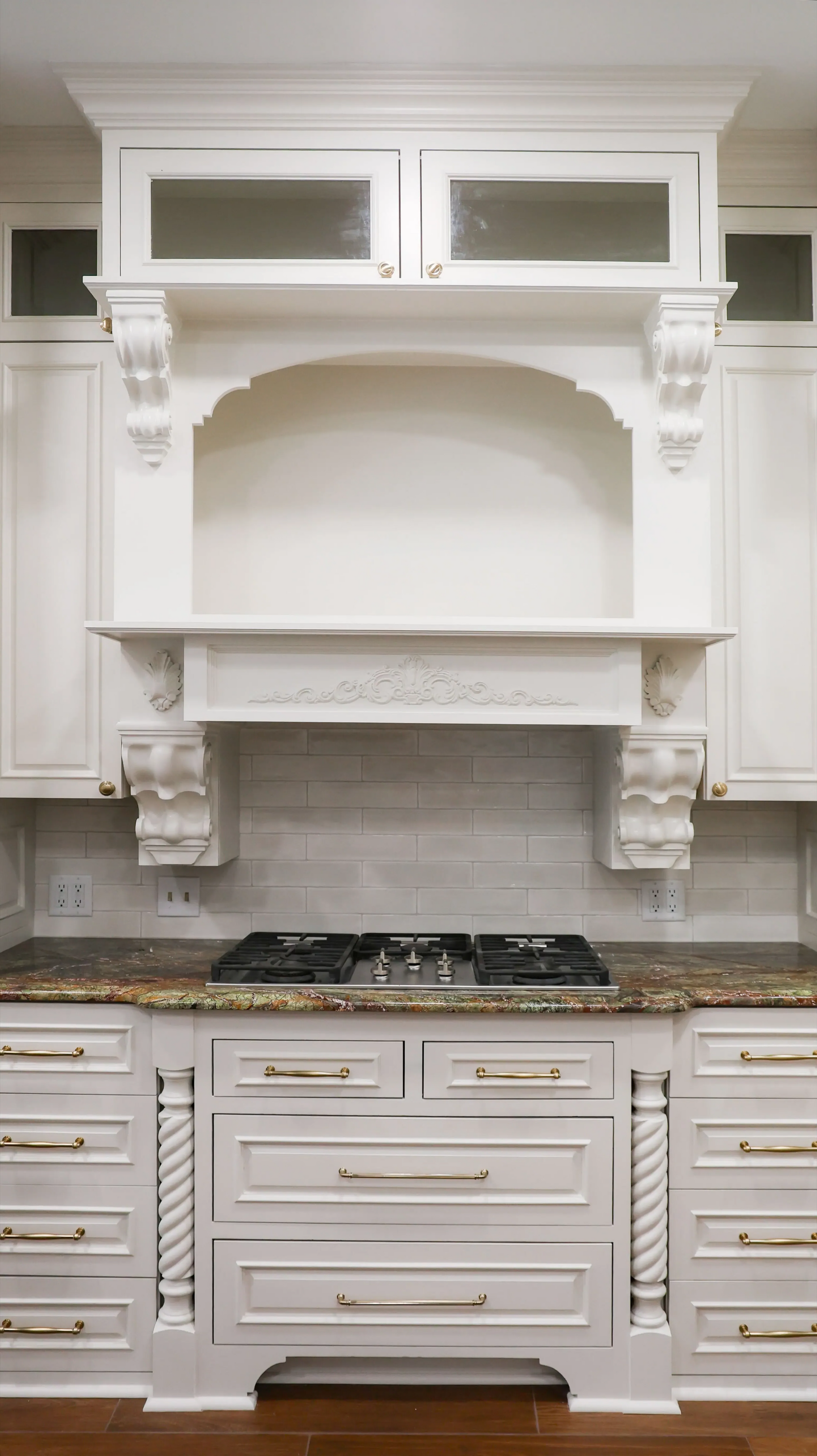 White kitchen range hood with decorative trim above a stove and marble backsplash