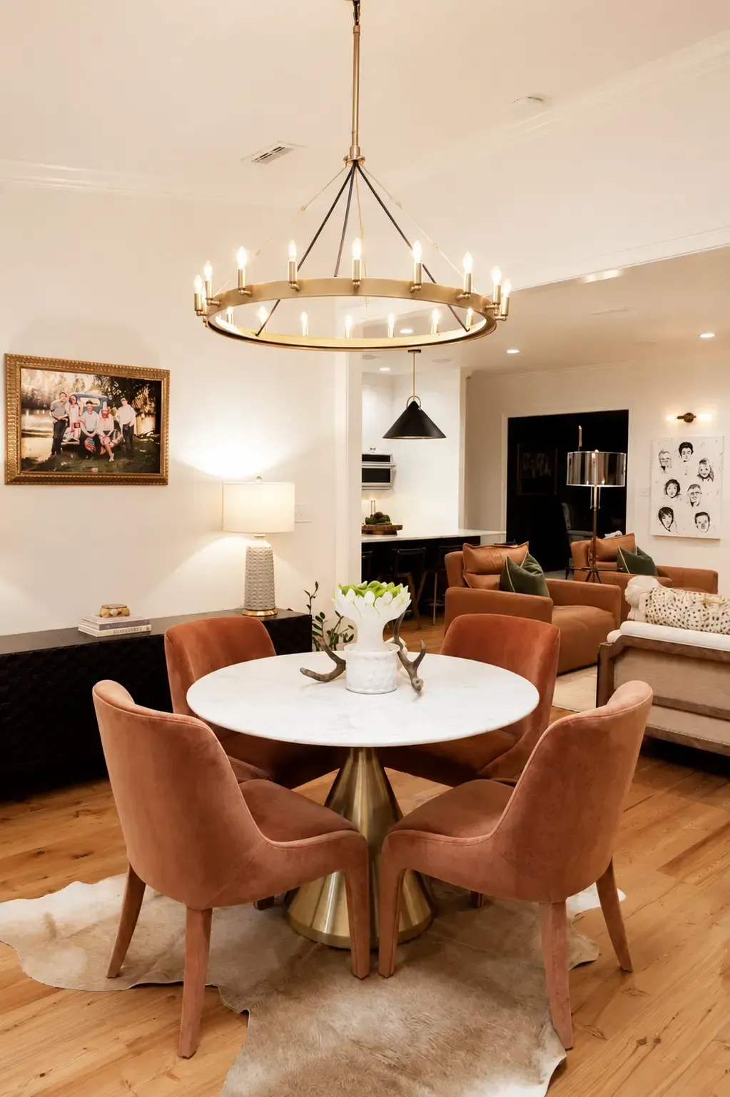 Elegant dining area with round marble table, rust chairs, and gold ring chandelier in open-plan living space