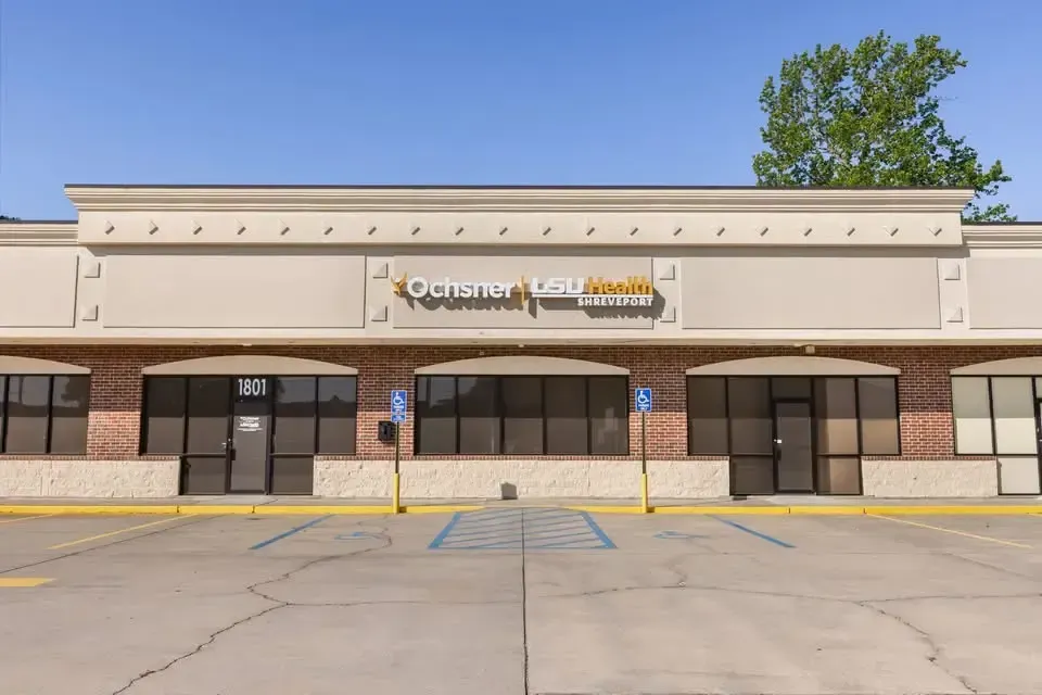 Empty storefronts in a beige strip mall with black awnings and a parking lot in front