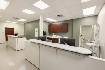 Bright medical reception area with white counters, cabinets, and a waiting room door.
