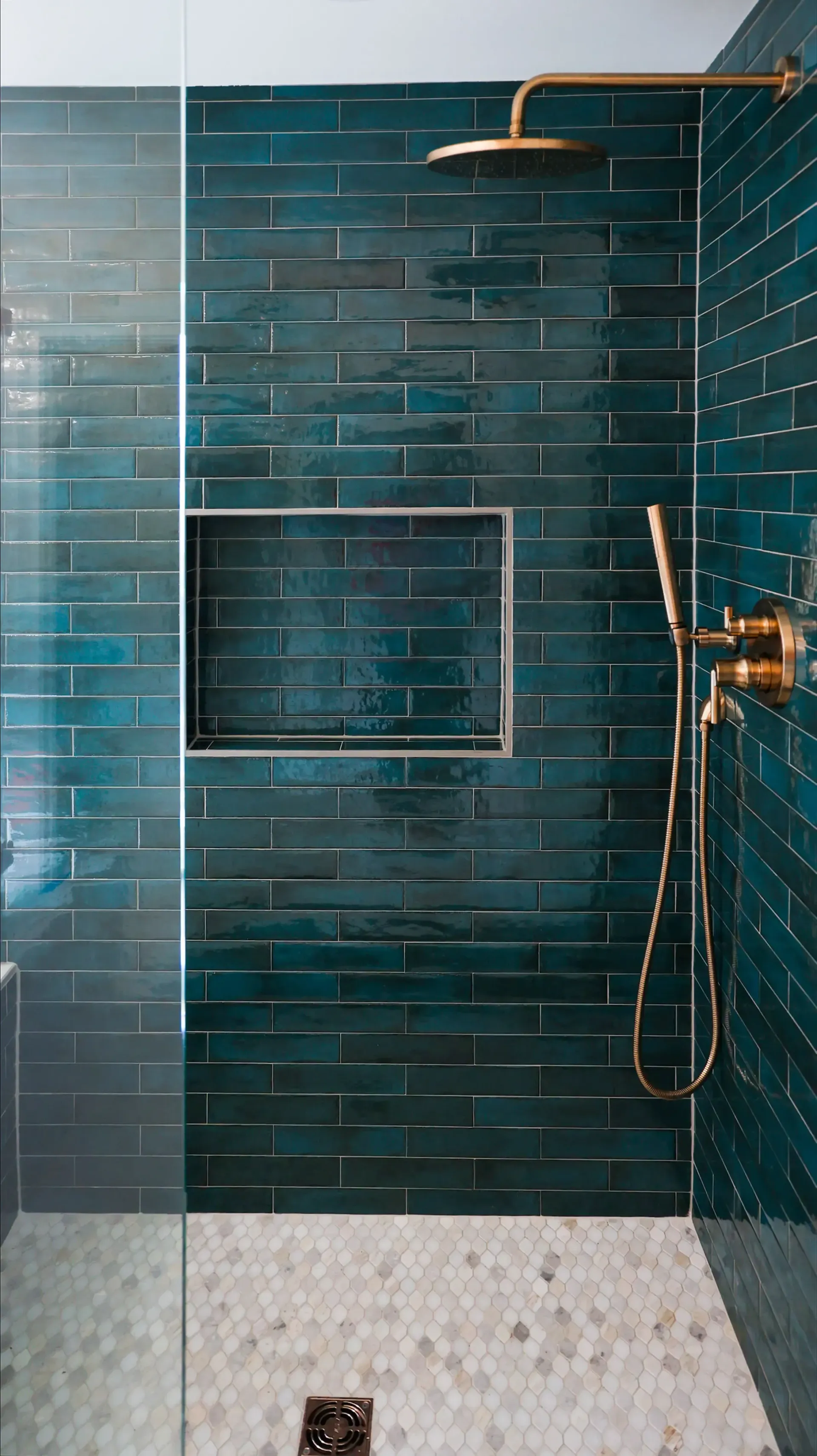 Modern shower with dark teal subway tile, white pebble floor, built-in niche, and brass shower fixtures